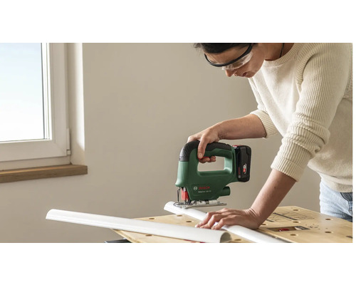 Person mit Schutzbrille schneidet mit einer Bosch Akku-Stichsäge ein weißes Kunststoffprofil auf einer Werkbank.