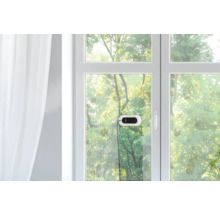 Fensterreinigungsroboter an einer Glasscheibe in einem hellen Raum mit Blick auf Bäume im Freien.