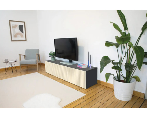 Modernes Wohnzimmer mit TV-Board mit vertikalen Holzlamellen, Fernseher, Sessel und Zimmerpflanze auf Holzfußboden.
