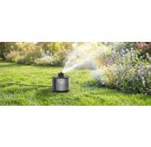 Smarter Rasensprenger Mowa bewässert ein Blumenbeet in einem sonnigen, gepflegten Garten mit feinem Wassernebel.