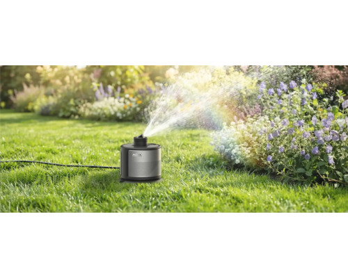 Smarter Rasensprenger Mowa bewässert ein Blumenbeet in einem sonnigen, gepflegten Garten mit feinem Wassernebel.