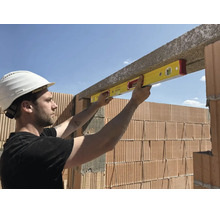 Bauarbeiter verwendet eine Wasserwaage zum Ausrichten eines Betonsturzes über einer Ziegelwand auf einer Baustelle.