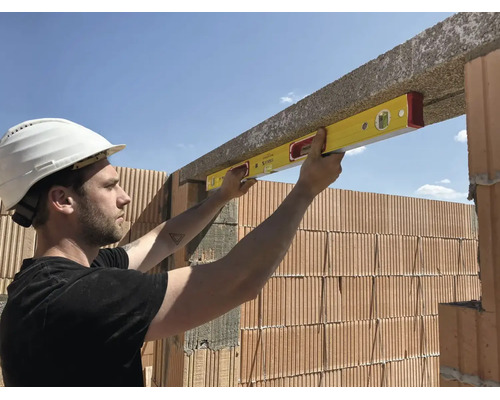 Bauarbeiter verwendet eine Wasserwaage zum Ausrichten eines Betonsturzes über einer Ziegelwand auf einer Baustelle.
