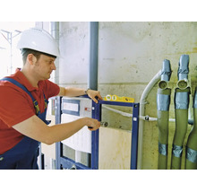 Handwerker montiert ein Vorwandelement für ein WC mit einer Wasserwaage auf einer Baustelle.