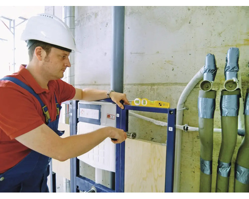 Handwerker montiert ein Vorwandelement für ein WC mit einer Wasserwaage auf einer Baustelle.