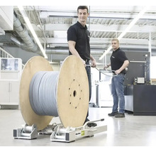 Zwei Männer in einer hellen Werkstatt bedienen eine große Kabeltrommel auf einer Roll-Profi Abwickelhilfe aus Metall.