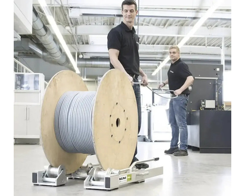 Zwei Männer in einer hellen Werkstatt bedienen eine große Kabeltrommel auf einer Roll-Profi Abwickelhilfe aus Metall.