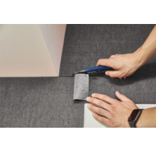 Zuschneiden von dunklem Vlies mit einem Cuttermesser an einer Wandecke.