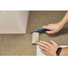 Eine Person schneidet einen strukturierten Bodenbelag aus Filz mit einem Cuttermesser zu.