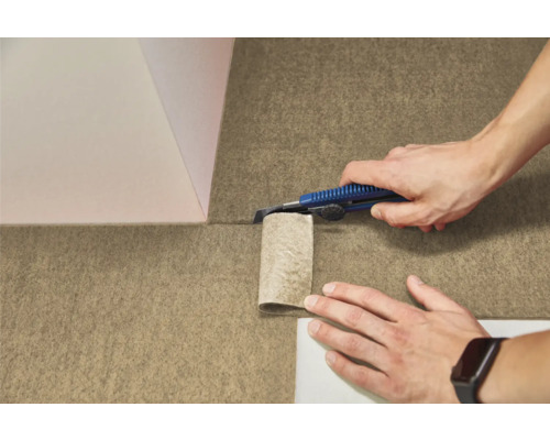 Eine Person schneidet einen strukturierten Bodenbelag aus Filz mit einem Cuttermesser zu.