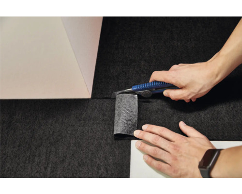Teppichboden verlegen: Zuschneiden des Belags mit einem Cuttermesser an einer Wandecke.