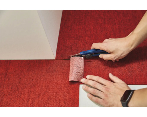 Person schneidet roten Teppichboden mit einem Teppichmesser zu.