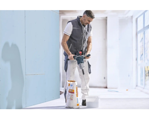 Handwerker rührt mit einem elektrischen Rührwerk Spachtelmasse in einem Eimer an, neben einem Sack Knauf Allround.