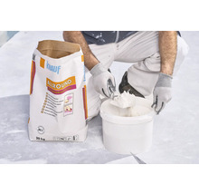 Handwerker entnimmt Spachtelmasse aus Eimer neben einem 20 Kilogramm Sack Knauf Allround 2 in 1 Universalspachtel.