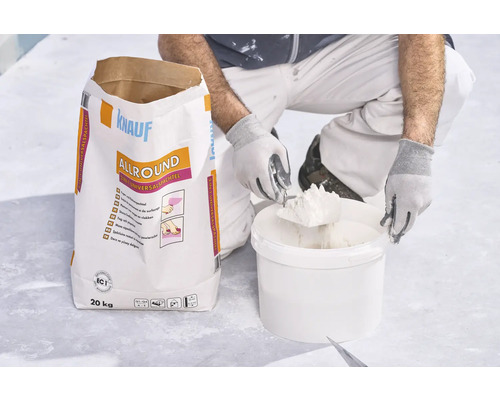 Handwerker entnimmt Spachtelmasse aus Eimer neben einem 20 Kilogramm Sack Knauf Allround 2 in 1 Universalspachtel.