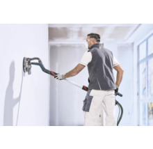 Handwerker glättet eine Wand mit einem Langhalsschleifer in einem hellen Innenraum.