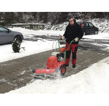 Ein Mann bedient eine motorisierte Kehrmaschine, um Schnee von einem gepflasterten Weg zu räumen.