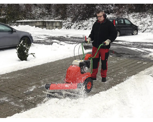 Ein Mann bedient eine motorisierte Kehrmaschine, um Schnee von einem gepflasterten Weg zu räumen.