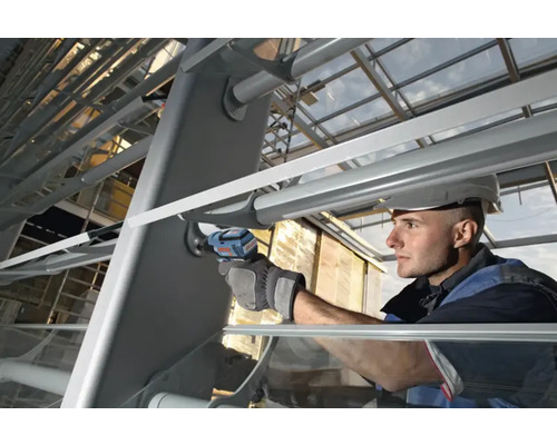 Handwerker mit Schutzhelm verwendet einen Akku-Schlagschrauber an einer Metallkonstruktion im Außenbereich.