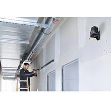 Handwerker nutzt Bosch Kreuzlinienlaser mit grünem Laserstrahl zur präzisen Ausrichtung einer Metallschiene an einer Trockenbauwand.