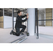 Ein Handwerker nutzt einen Bosch Kreuzlinienlaser, um eine vertikale grüne Laserlinie zur Markierung auf eine Betonsäule zu projizieren.