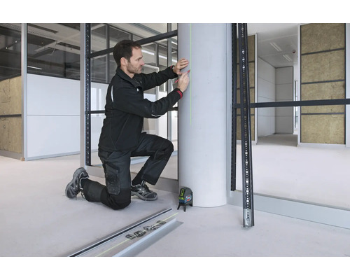 Ein Handwerker nutzt einen Bosch Kreuzlinienlaser, um eine vertikale grüne Laserlinie zur Markierung auf eine Betonsäule zu projizieren.