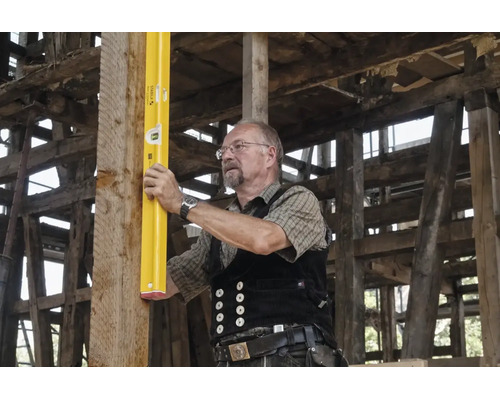 Ein Handwerker richtet mit einer Stabila Wasserwaage einen vertikalen Holzbalken in einem Fachwerkhaus aus.