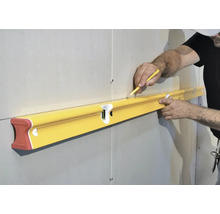 Eine Person hält eine lange Wasserwaage an eine Trockenbauwand und markiert mit einem Bleistift eine waagerechte Linie.