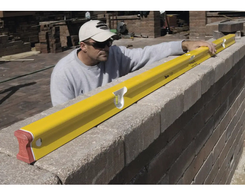 Handwerker prüft mit einer gelben Wasserwaage die Ausrichtung einer Steinmauer auf einer Baustelle.