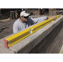 Handwerker prüft mit einer gelben Wasserwaage die Ausrichtung einer Steinmauer auf einer Baustelle.