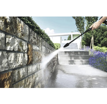 Reinigung einer Natursteinmauer im hellen Garten mit einem Hochdruckreiniger, neben Steintreppen und Lavendel.