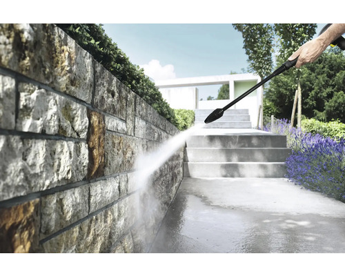 Reinigung einer Natursteinmauer im hellen Garten mit einem Hochdruckreiniger, neben Steintreppen und Lavendel.