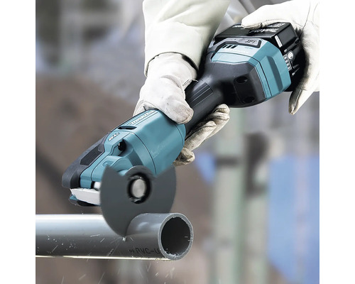 Makita Akkumulator-Multischleifer schneidet ein graues Kunststoffrohr, Person trägt Arbeitshandschuhe.