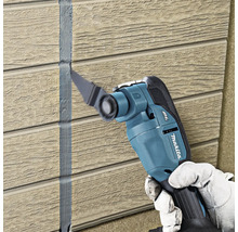 Makita Multifunktionswerkzeug entfernt Dichtstoff zwischen Wandpaneelen mit Holzstruktur.