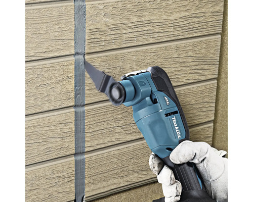 Makita Multifunktionswerkzeug entfernt Dichtstoff zwischen Wandpaneelen mit Holzstruktur.