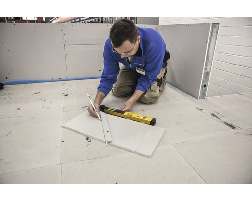 Handwerker markiert Gipskartonplatte mit Bleistift und Metalllineal neben einer digitalen Wasserwaage.