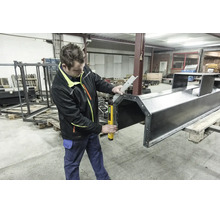 Handwerker in einer Werkstatt verwendet einen digitalen Winkelmesser, um eine große Metallkonstruktion auf einer Palette präzise zu messen.