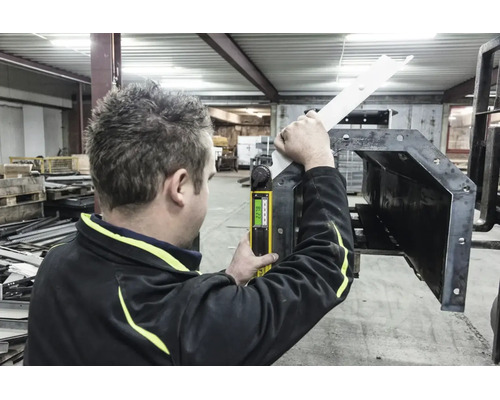 Eine Person verwendet einen digitalen Winkelmesser zum Messen eines Metallwerkstücks in einer hellen Werkstatt.