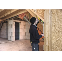 Handwerker verwendet eine digitale Wasserwaage mit STABILA Logo an einem Holzbalken in einem Rohbau mit Porenbetonwänden und Grobspanplatten.