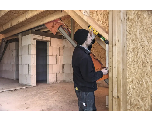 Handwerker verwendet eine digitale Wasserwaage mit STABILA Logo an einem Holzbalken in einem Rohbau mit Porenbetonwänden und Grobspanplatten.
