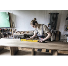 Handwerkerin prüft mit einer Wasserwaage die Ausrichtung einer Holzplatte in einer gut organisierten Werkstatt.