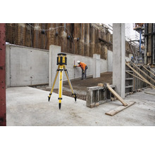 Stabila Rotationslaser auf Stativ auf einer Baustelle mit einem Bauarbeiter, der Messungen an einer Betonwand vornimmt.