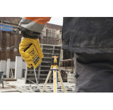 Hand mit Stabila Fernbedienung für einen Rotationslaser auf einer Baustelle, im Hintergrund ein Laser auf einem Stativ.