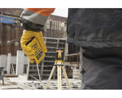 Hand mit Stabila Fernbedienung für einen Rotationslaser auf einer Baustelle, im Hintergrund ein Laser auf einem Stativ.