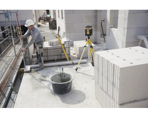 Bauarbeiter nutzt Rotationslaser auf Stativ zur Vermessung auf einer Baustelle mit Porenbetonsteinen.
