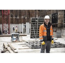 Bauarbeiter auf einer Baustelle mit weißem Schutzhelm, Warnschutzjacke und Arbeitshandschuhen.