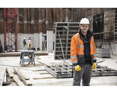 Bauarbeiter auf einer Baustelle mit weißem Schutzhelm, Warnschutzjacke und Arbeitshandschuhen.