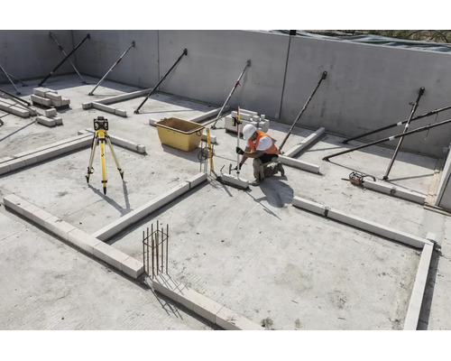 Bauarbeiter auf einer Baustelle nutzt einen Rotationslaser und eine Messlatte zum Ausrichten von Mauersteinen auf dem Betonfundament.