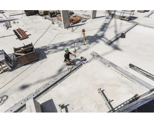 Bauarbeiter auf einer Betonbaustelle verwendet einen Rotationslaser und eine Messlatte zur Nivellierung.