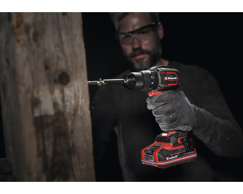 Einhell Akku-Bohrschrauber im Einsatz an einem Holzbalken, geführt von einer Person mit Arbeitshandschuh und Schutzbrille.